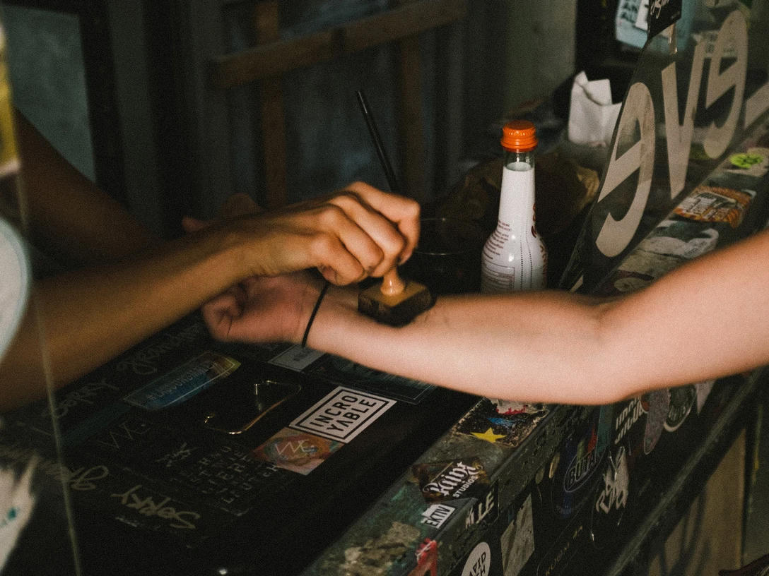 Club Zwei Hände treffen sich für einen Armstempel in einem schummrigen Raum voller Aufkleber.Two hands meet for an arm stamp in a dimly lit room full of stickers.