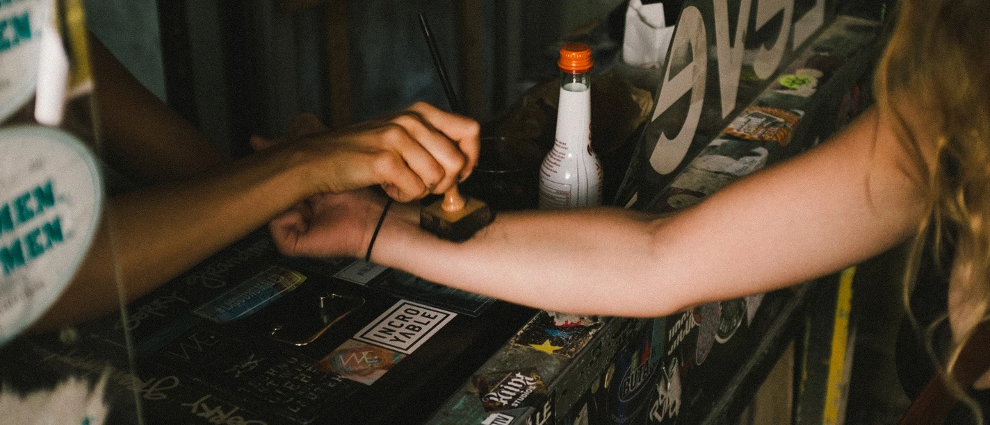 Club Zwei Hände treffen sich für einen Armstempel in einem schummrigen Raum voller Aufkleber.