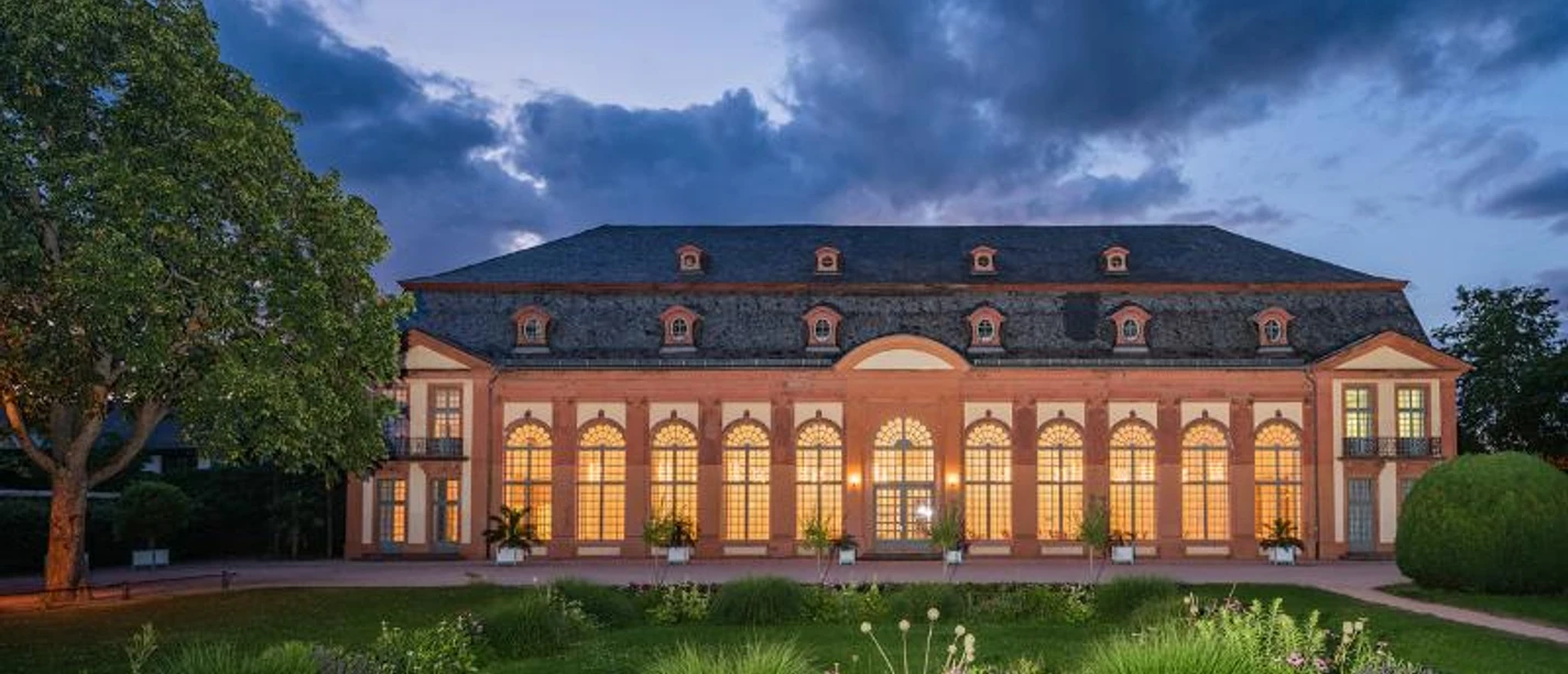 Orangerie Orangerie: Prunkvolles historisches Gebäude bei Dämmerung mit erleuchteten Fenstern.