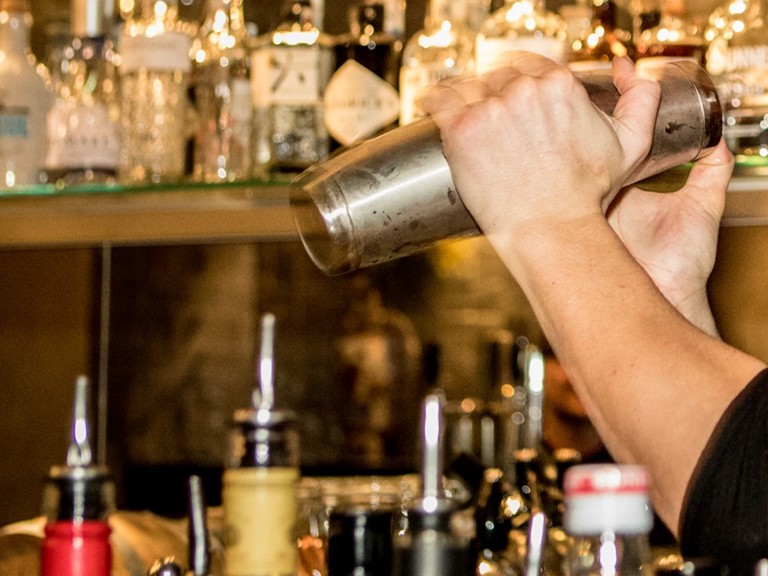 Bar Ein Barkeeper schüttelt einen Edelstahl-Shaker, im Hintergrund sind Flaschen zu sehen.A bartender shakes a stainless steel shaker, bottles can be seen in the background.