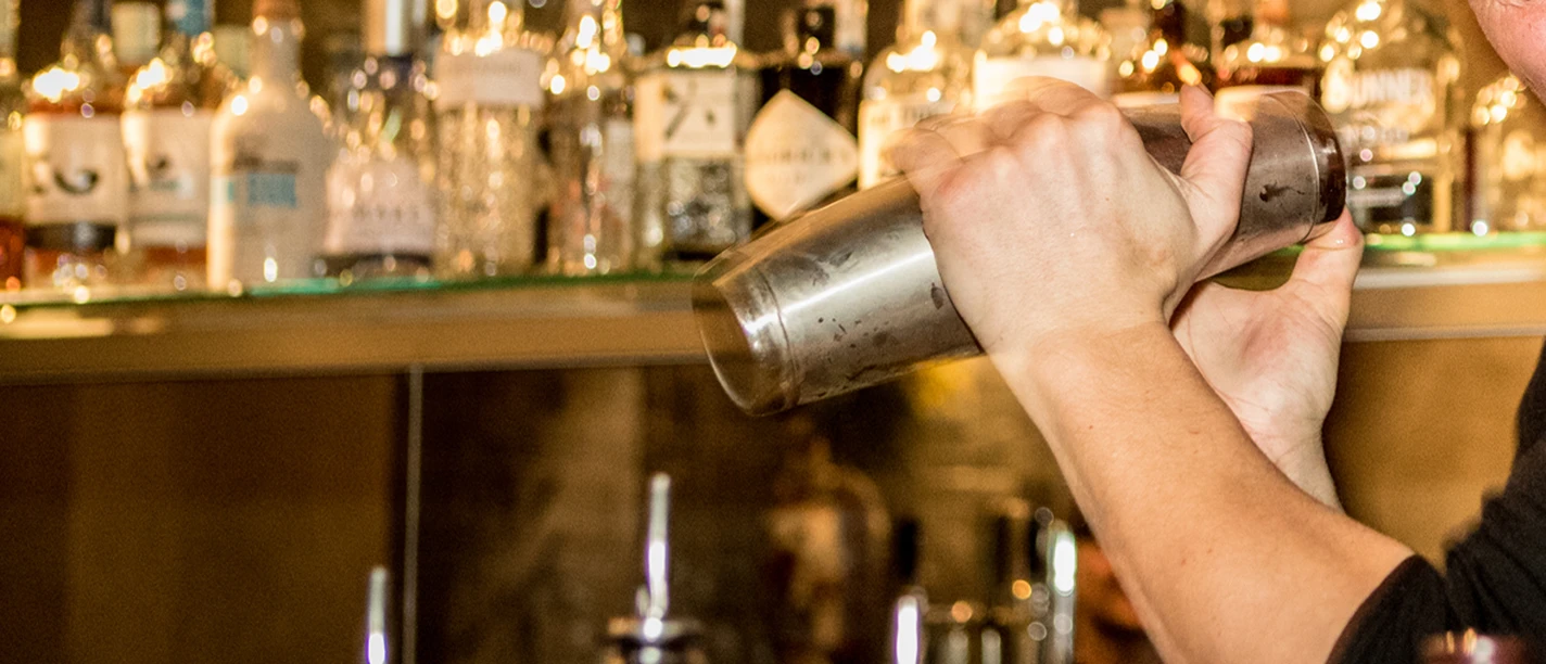 Bar A bartender shakes a stainless steel shaker, bottles can be seen in the background.