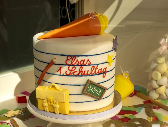 Madame Miammiam Bunter Einschulungskuchen mit Tafel, Schultüte und Schokolade als Verzierung auf einer Tortenplatte.Colorful first school cake with blackboard, school cone and chocolate as decoration on a cake plate.