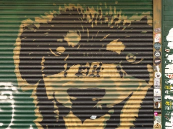 Frieda Bar Ein Graffiti mit dem Bildnis eines freundlich wirkenden Bären auf einem Rolltor, umgeben von Stickern.A graffiti with the image of a friendly-looking bear on a roller shutter, surrounded by stickers.