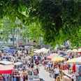 Flea market in Cologne-Nippes Eine lebendige Flohmarkt-Szene voller bunter Stände und emsiger Menschen unter schattenspendendem Laub.A lively flea market scene full of colorful stalls and busy people under shady foliage.