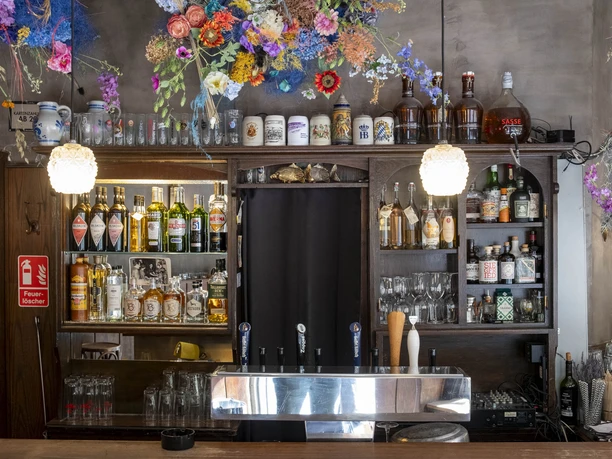 Forelle Blau Barbereich mit farbenfrohem Blumenschmuck und diversen Getränken; warmes und einladendes Ambiente.