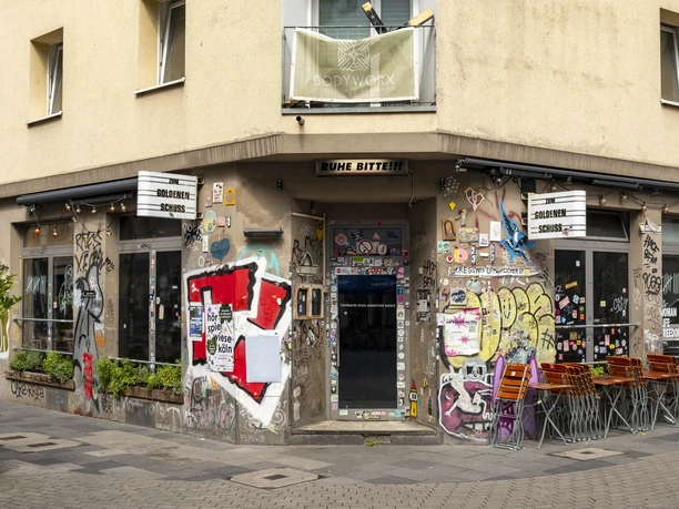 Zum Goldenen Schuss Entrance of the pub full of colorful graffiti, with several tables outside.
