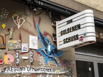 Zum Goldenen Schuss Bunte Street-Art mit Vogelmotiv und Graffiti an einer Hauswand im urbanen Köln.Colorful street art with a bird motif and graffiti on a house wall in urban Cologne.