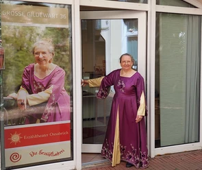 Erzähltheater Osnabrück Frau im violetten Kleid lächelt einladend, steht vor dem Erzähltheater Osnabrück.