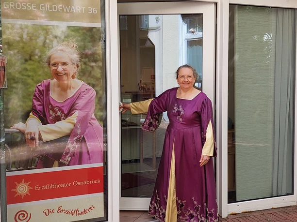 Frau im violetten Kleid lächelt einladend, steht vor dem Erzähltheater Osnabrück.