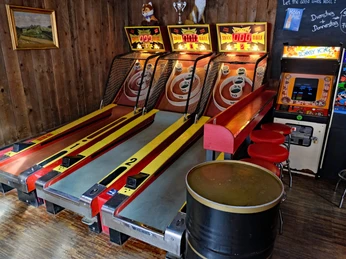 Skeeballbahnen in der Red Fox Bar Zwei Skee-Ball-Automaten stehen in einer Holzwand-Nische, daneben ein Donkey Kong Arcade Game.Two Skee-Ball machines stand in a wooden wall niche, next to a Donkey Kong arcade game.