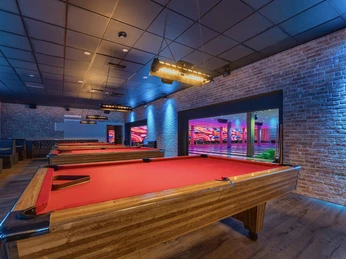 Billardtische bei West Bowling Ein moderner Billardraum mit drei leuchtend roten Tischen, umgeben von gemauerten Wänden und stimmungsvollem Licht.A modern billiard room with three bright red tables, surrounded by brick walls and atmospheric lighting.