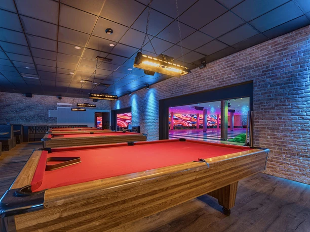 Billiard tables at West Bowling A modern billiard room with three bright red tables, surrounded by brick walls and atmospheric lighting.