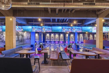 Bowling lanes at Underlux Interior of the Underlux bowling center with blue and purple lights, tables in the foreground.