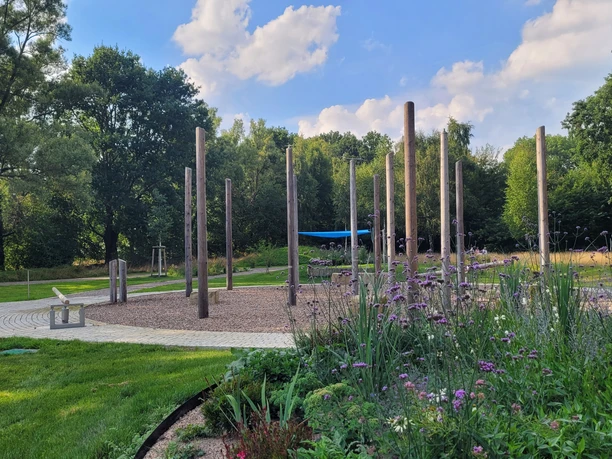 Wasserspielplatz Kurpark Levern Ein Wasserspielplatz mit hölzernen Standelementen, umgeben von gepflegten Grünflächen und Bäumen.