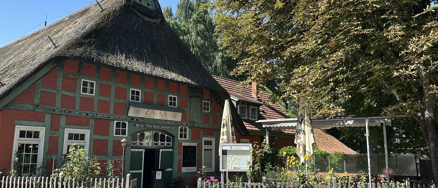 Zaika Restaurant und Tapas Bar von außen Fachwerkhaus mit Reetdach und grünen Balken, davor Terrasse mit Sonnenschirmen und Blumen.