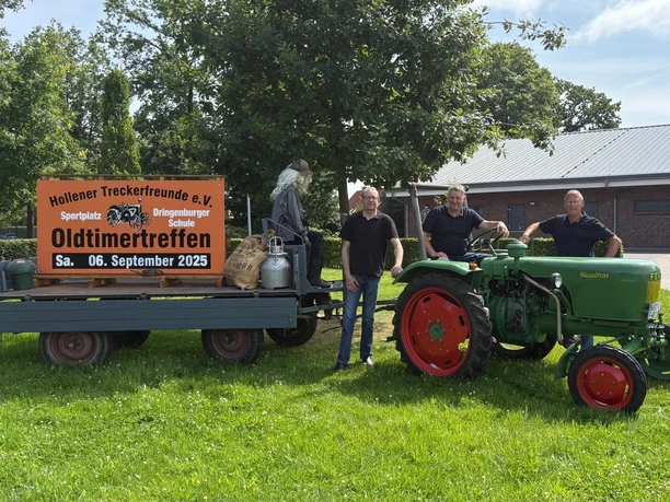 Grüne Wiese mit drei lächelnden Personen neben einem grünen Traktor und einem großen Schild.