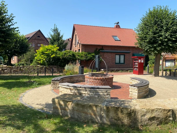 Roter Klinkerbau im Hintergrund mit einem kleinen Backsteingrillplatz und Bänken im Vordergrund.