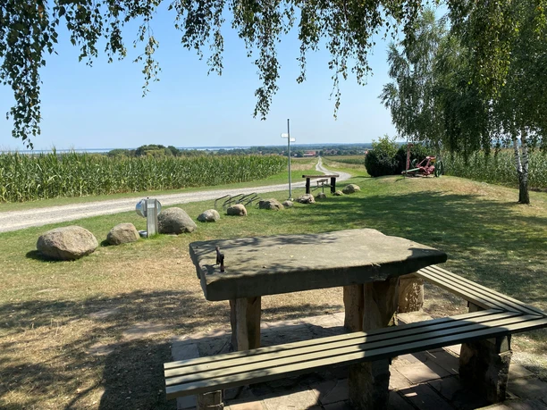 Picknicktisch aus Holz vor einem Weg, umgeben von Feldern, Felsen und Bäumen mit weitem Ausblick.