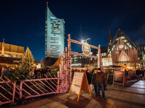 Entrance to the Finnish village with log cabin and tent in the evening with the city skyscraper in the background