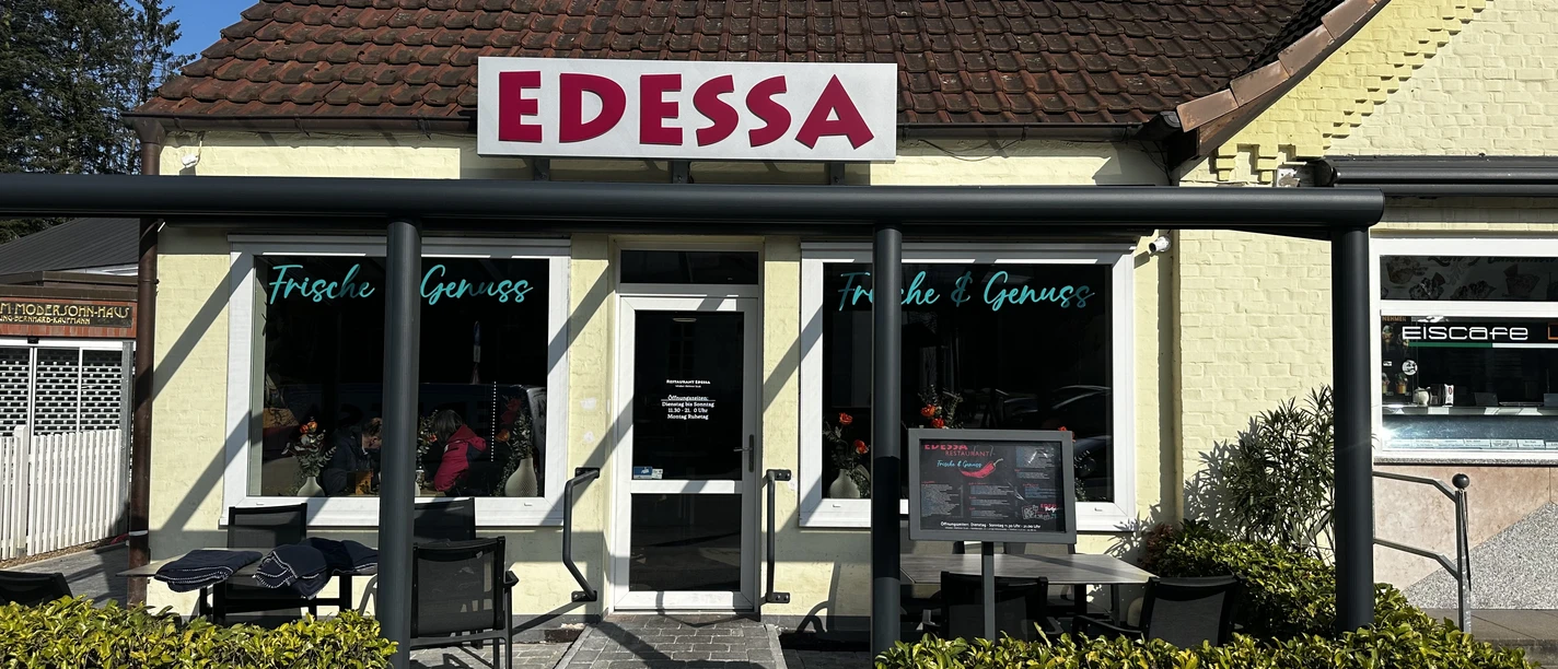 Edessa Schnellrestaurant Gelb verputztes Schnellrestaurant mit rotem Schriftzug Edessa und kleiner Terrasse mit Sitzplätzen.