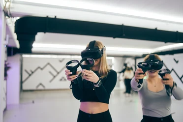 7th Space Cologne Two people are standing in a bright room wearing VR headsets and controllers.