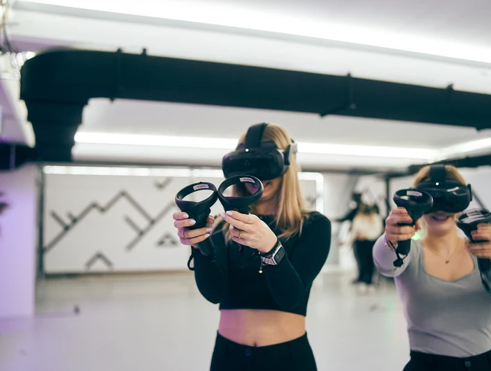 7th Space Köln Zwei Personen stehen in einem hellen Raum und tragen VR-Headsets und Controller.Two people are standing in a bright room wearing VR headsets and controllers.