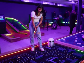 7th Space Köln Auf farbenfrohem Indoor-Minigolfplatz steht eine Person mit Minigolf-Schläger vor einem futuristisch gestalteten Hindernis.A person with a minigolf club stands in front of a futuristically designed obstacle on a colorful indoor minigolf course.