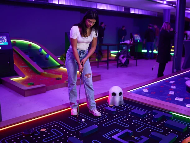 7th Space Köln Auf farbenfrohem Indoor-Minigolfplatz steht eine Person mit Minigolf-Schläger vor einem futuristisch gestalteten Hindernis.