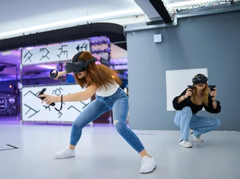 7th Space Köln Zwei Personen mit Virtual-Reality-Headsets und Controllern tauchen in eine immersive VR-Erfahrung ein.Two people with virtual reality headsets and controllers immerse themselves in an immersive VR experience.