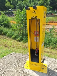 Radservice-Station in Wiehl Gelbe ADAC Radservice-Station mit Reparaturwerkzeug und Luftpumpe, umgeben von Bäumen.