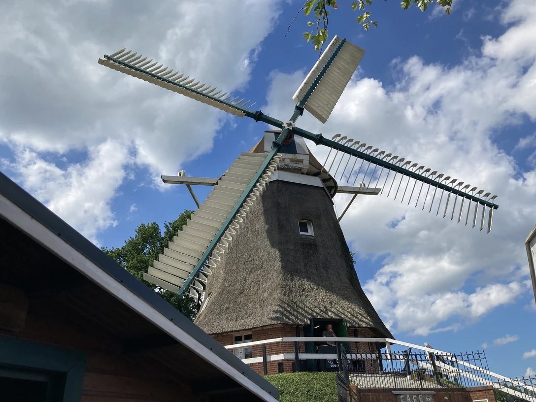 IMG_5578.JPG Traditionelle holländische Windmühle mit Strohdach und großen Flügeln vor blauem Himmel mit Wolken