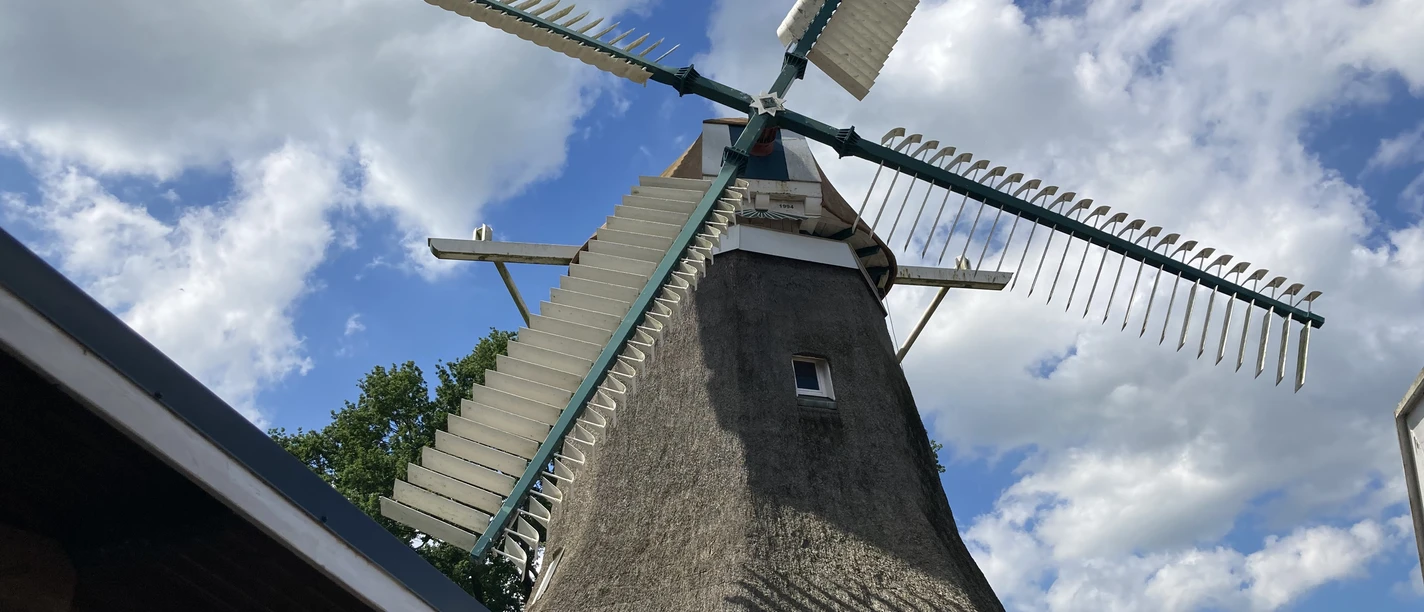 IMG_5578.JPG Traditionelle holländische Windmühle mit Strohdach und großen Flügeln vor blauem Himmel mit Wolken