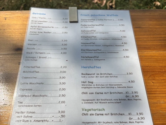 Speisekarte im Freien mit Getränken, Waffeln und herzhaften Snacks wie Brötchen und Chili.