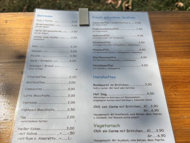 Speisekarte im Freien mit Getränken, Waffeln und herzhaften Snacks wie Brötchen und Chili.
