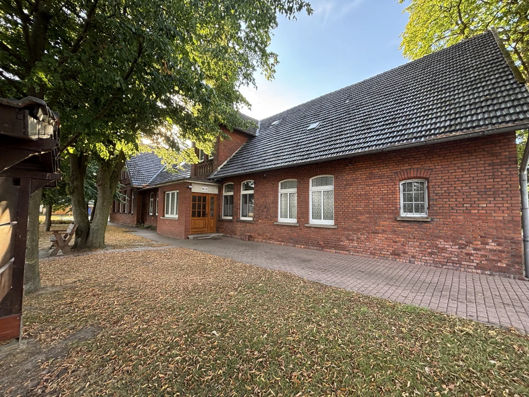 Rotes Backsteingebäude mit schrägem Dach inmitten von Bäumen, umgeben von herbstlichem Laub.