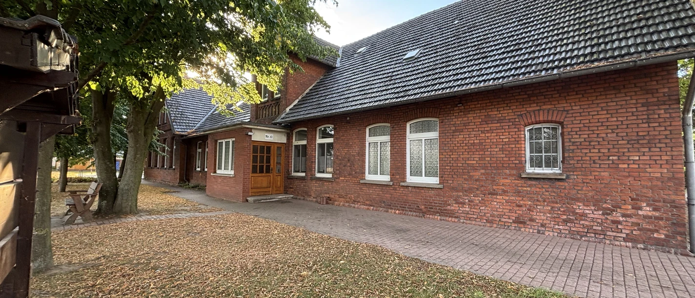 Rotes Backsteingebäude mit schrägem Dach inmitten von Bäumen, umgeben von herbstlichem Laub.