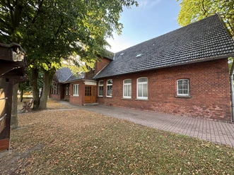 Alte Schule Wietersheim Nr. 3 Rotes Backsteingebäude mit schrägem Dach inmitten von Bäumen, umgeben von herbstlichem Laub.