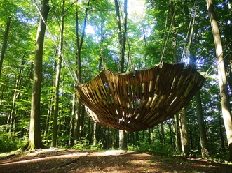 Mit Seilen an Bäumen befestigt Holzkonstruktion in Form eines großen Nestes, in welchem mehrere Personen Platz haben.