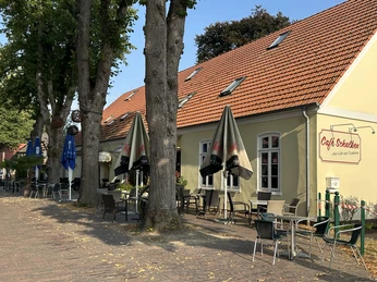 Café Schulken in der Bergstraße Gelbes Caféhaus mit rotem Ziegeldach, Außenterrasse unter Bäumen mit Tischen und Sonnenschirmen.