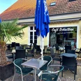 Café Schulken Außenbereich des Café Schulken mit schwarzen Sitzmöbeln, blauen Sonnenschirmen und Palme.