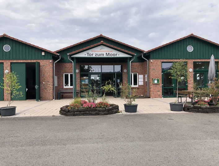 Infozentrum "Tor zum Moor" Brick building with green roof and glass fronts, surrounded by plants, with sign "Tor zum Moor".