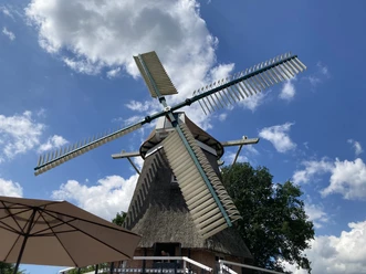 IMG_5564.JPG Traditionelle holländische Windmühle mit Strohdach unter blauem Himmel mit Wolken, Sonnenschirm im Vordergrund