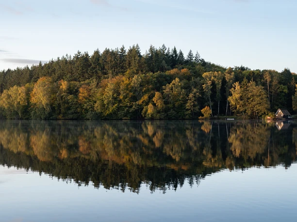 Der ruhige Salemer See mit Wald und kleinem Bootshaus, spiegelt im klaren Wasser.