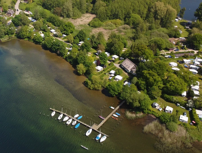 Campingplatz Zur schönen Aussicht_Luftaufnahme Luftaufnahme des Campingplatzes am Seeufer mit Bootssteg, umgeben von Wald und vielen Wohnmobilen.