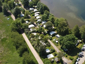 Campingplatz Zur schönen Aussicht_Luftaufnahme Campingplatz am Seeufer mit Bäumen und Wohnmobilen, neben einem Bootssteg, aus der Luft gesehen.