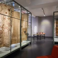 Ausstellung SCHUTZ Foto Tom Dachs.jpg Ausstellung mit antiken Textilien in Glasvitrinen in einem modernen Museumssaal.