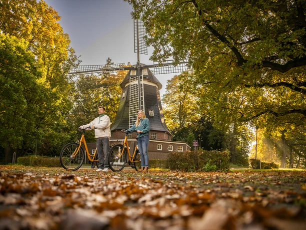 Höltingmühle, Meppen Zwei Personen mit Fahrrädern vor der historischen Höltingmühle in Meppen im herbstlichen Licht