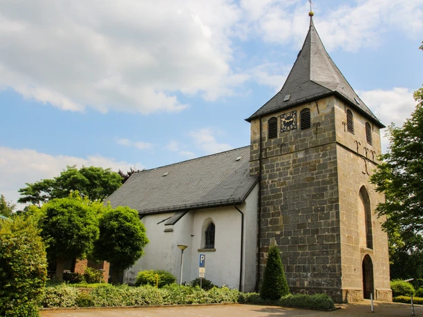 Kirche St. Vitus in Bokeloh Historische Kirche mit hohem grauen Turm, Uhrziffernblatt und weißem Kirchenschiff unter blauem Himmel.