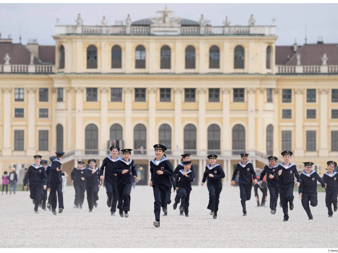 Wiener Sängerknaben - Weihnachtskonzert Eine Gruppe von uniformierten Kindern rennt freudig durch den weitläufigen Vorhof eines Palastes.