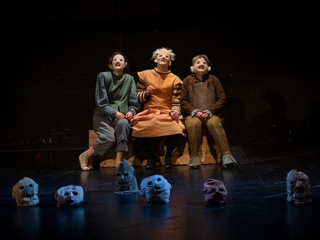 Schauspiel Leipzig spielt Hamlet Frei nach William Shakespeare Drei Darsteller mit ausdrucksstarken Masken sitzen auf der Bühne, von Totenkopfmasken umgeben.